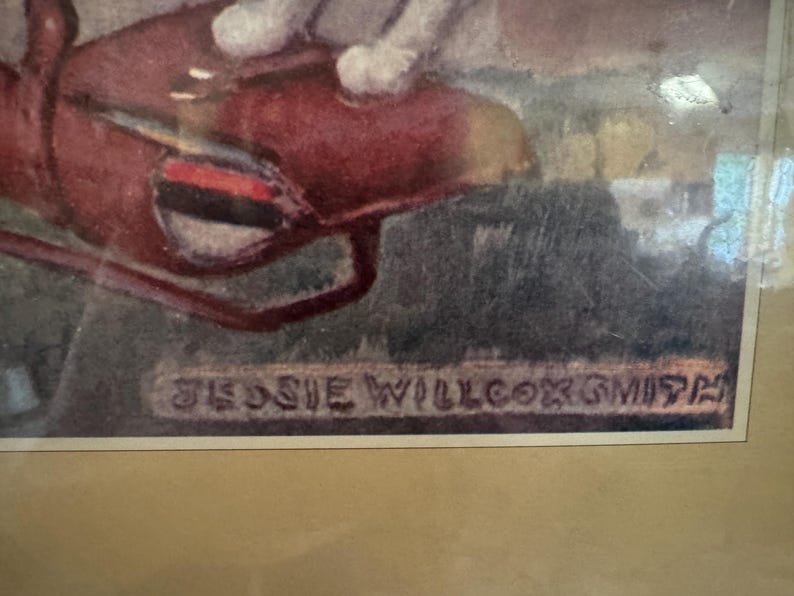 May include: Framed artwork featuring a watercolor painting with a red object and the artist's signature, "JESSIE WILLCOX SMITH." The artwork is set against a muted background, with a tan mat and a gold-toned frame.