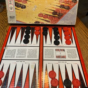 May include: A vintage Milton Bradley Backgammon and Acey Deucy game board set. The game board is red and black with white triangles. The game pieces are red and black. The box is brown with white text.