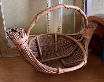 May include: A brown woven wicker basket with a unique curved handle. The basket is made of natural materials and has a rustic, handmade look.
