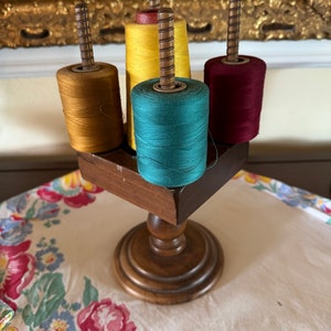 May include: Wooden spool holder with four spools of thread in yellow, teal, brown, and red.