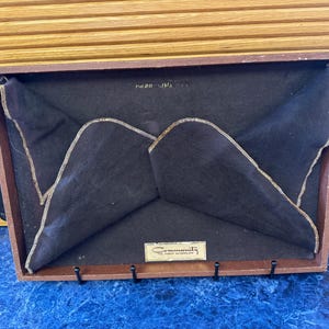 May include: A wooden tray with a brown fabric lining and four hooks. The tray has the text "Community" and "The Great Exchange" printed on a label.