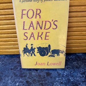 May include: A yellow book cover with the title "FOR LAND'S SAKE" in black and pink lettering. The book is a personal story of pioneer adventure by Joan Lowell. The cover features a black and white illustration of a wagon train traveling through a landscape.