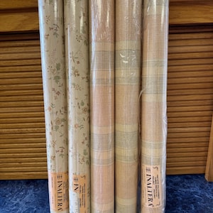 May include: Five rolls of wallpaper, some wrapped in clear plastic. Two rolls feature a floral pattern with green and pink accents on a cream background. The other three rolls have a striped design in shades of peach, beige, and light green.