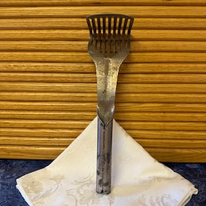 May include: A vintage metal potato masher with a long handle and a slotted head. The masher is rusty and has been used many times.