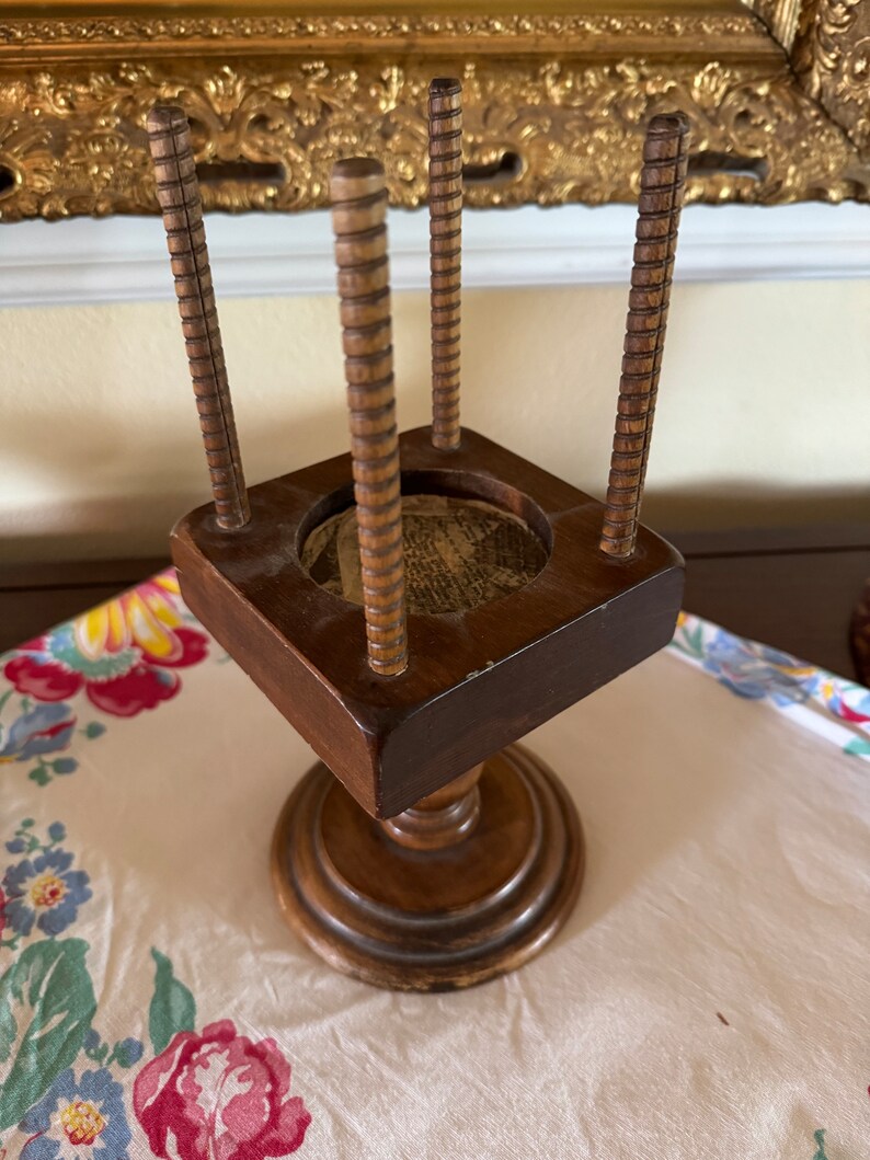 May include: A wooden stand with four spindles and a square top. The stand has a turned base and is made of dark wood.