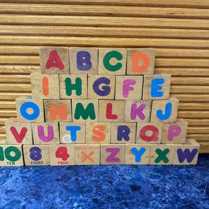 May include: Wooden alphabet blocks with colorful letters and numbers. The blocks are arranged in a stacked formation, displaying the letters A through W, and the numbers 4, 8, and 10. The blocks are on a blue surface.