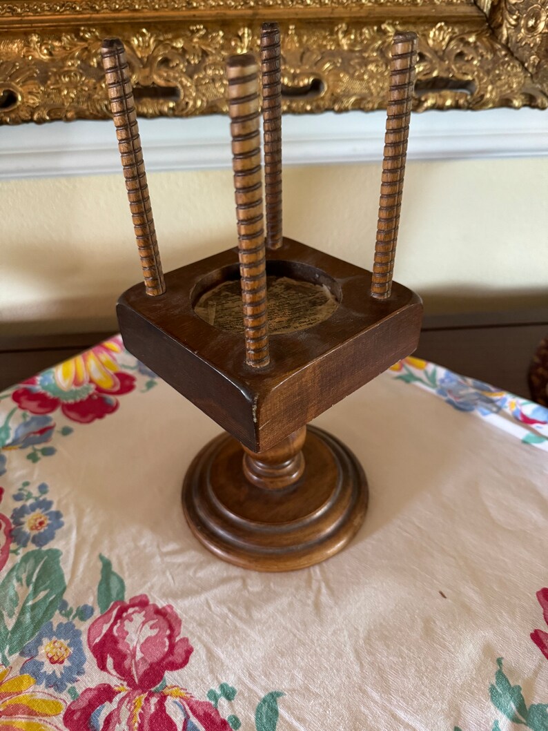 May include: A wooden stand with four vertical dowels and a square base. The stand has a turned pedestal base.