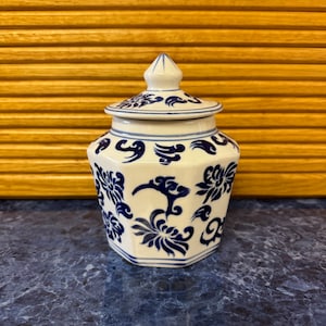 May include: A white ceramic jar with a blue and white floral design. The jar has a lid with a pointed top.