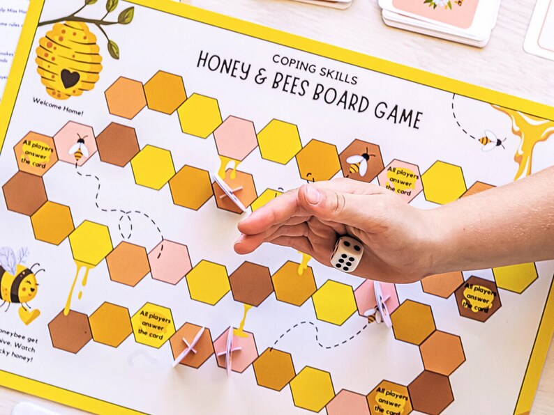 K&ouml;nnte beinhalten: Ein Honig & Bienen Brettspiel f&uuml;r Bew&auml;ltigungsf&auml;higkeiten. Das Spielbrett hat ein Wabenmuster mit gelben und braunen sechseckigen Feldern. Das Spiel beinhaltet einen W&uuml;rfel und Karten. Der Text auf dem Brett lautet "Bew&auml;ltigungsf&auml;higkeiten Honig & Bienen Brettspiel".