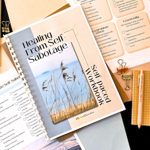 a self-healing workbook titled "Healing From Self-Sabotage" with a list of self-healing techniques and a calming nature scene. The workbook is surrounded by other materials, including a pen, a stapler, and a piece of paper.
