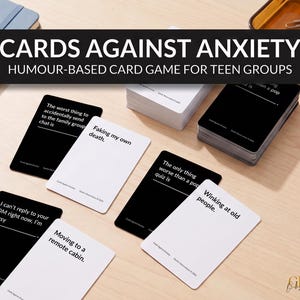 May include: Cards Against Anxiety humor-based card game for teen groups featuring black and white playing cards with text prompts and responses like Faking my own death, Moving to a remote cabin, and Winking at old people on a light surface.