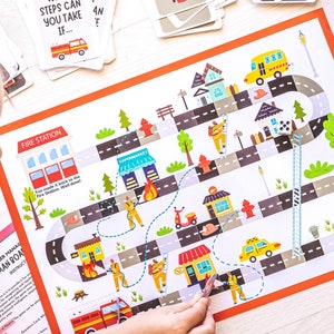 May include: A colorful board game with a fire station theme. The game board features a winding road with houses, a supermarket, a fire hydrant, and a fire truck. A child is playing the game with a die and a marker.
