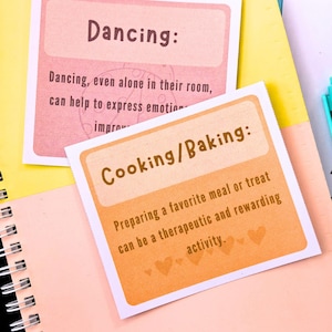 two cards with text on them, placed on a yellow and pink notebook.