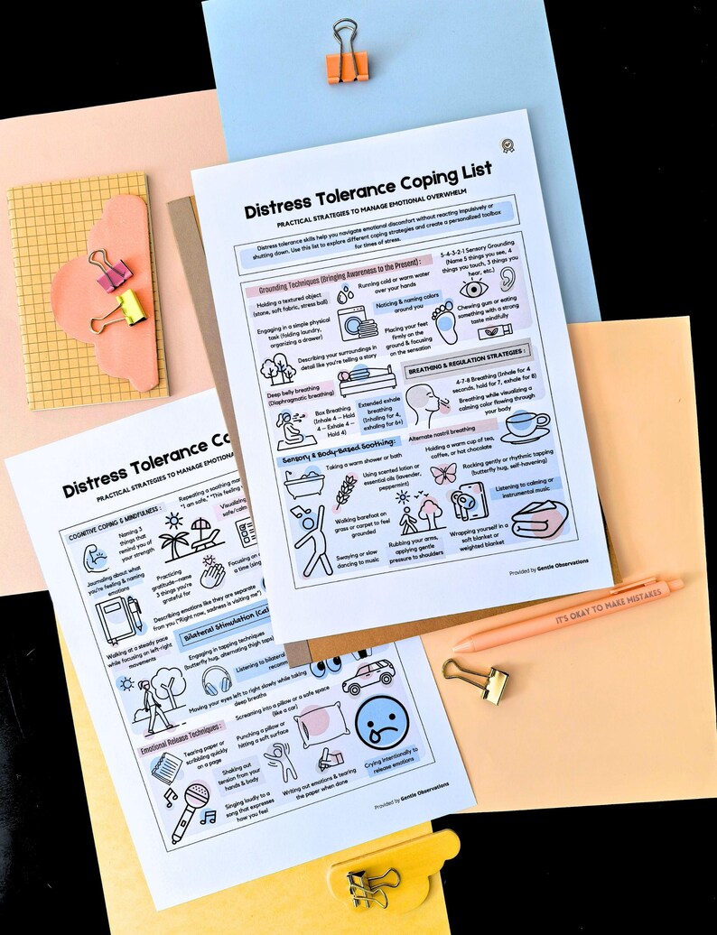 May include: A flat lay featuring two printed sheets titled "Distress Tolerance Coping List" with coping strategies, alongside a peach pen, paper clips, and a notepad. The pen reads "IT'S OKAY TO MAKE MISTAKES". The background is a mix of peach, blue, and yellow.