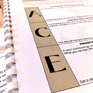 a close-up view of a spiral-bound notebook or folder with a page featuring the word "ACE" prominently displayed.