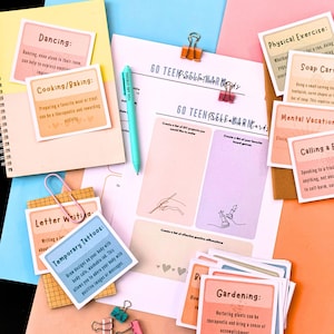 various items related to self-care and personal development, including a notebook, a pen, a sticky note, a spiral notebook, and several cards with different activities and prompts.