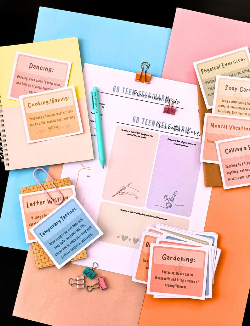 various items related to self-care and personal development, including a notebook, a pen, a sticky note, a spiral notebook, and several cards with different activities and prompts.