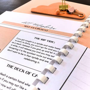 a spiral-bound notebook with a page titled "The Rip Tide" and a binder clip on top of it. The notebook appears to be open, and the page contains text that is partially visible.