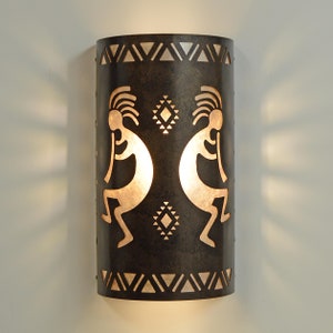 May include: A brown metal wall sconce with a cutout design of two Native American dancers. The sconce has a geometric pattern around the top and bottom.
