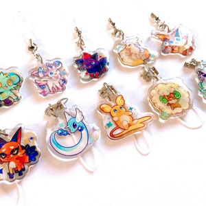 Puede incluir: Un conjunto de diez amuletos de personajes de estilo anime de colores con llaveros de plástico transparente. Los amuletos presentan varios personajes de la franquicia Pokémon, incluyendo Eevee, Sylveon y Glaceon.