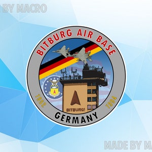 May include: A gray and white circular emblem with the text "Bitburg Air Base 1952 - 1994 Germany" around the edge. The emblem features a control tower, two fighter jets, and the German flag.