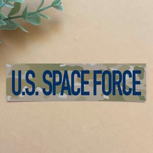May include: A camouflage-patterned patch with the text "U.S. SPACE FORCE" in blue lettering.