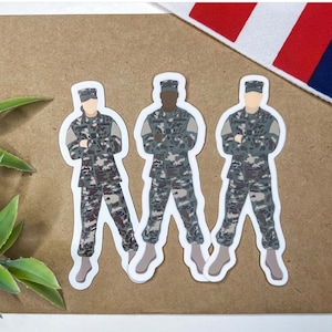 May include: Three camouflage patterned stickers of military personnel standing with their arms crossed. The stickers are on a brown background.