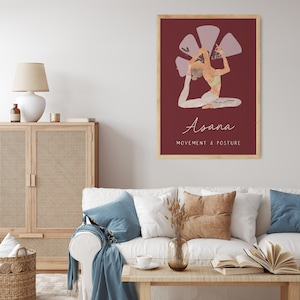 May include: A framed art print featuring a yoga pose illustration. The artwork depicts a person in a seated backbend pose against a deep red background. The word "Asana" is written in cursive, with "Movement & Posture" below.