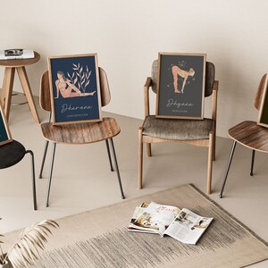 May include: Four framed yoga art prints featuring illustrations of yoga poses and associated Sanskrit terms. The prints are in wooden frames and are displayed on different chairs. The color palette includes teal, navy, gray, and olive green backgrounds with beige and peach figures.