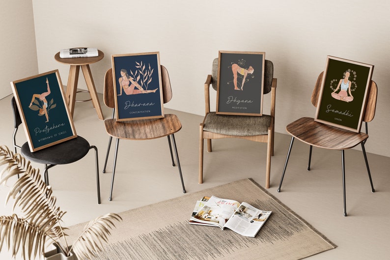 May include: Four framed yoga art prints featuring illustrations of yoga poses and associated Sanskrit terms. The prints are in wooden frames and are displayed on different chairs. The color palette includes teal, navy, gray, and olive green backgrounds with beige and peach figures.