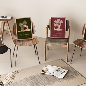 May include: Four framed yoga art prints, each featuring a different pose and corresponding text. The prints are displayed on various chairs, with a neutral-toned rug and a small side table in the background. The color palette includes muted greens, reds, and yellows.