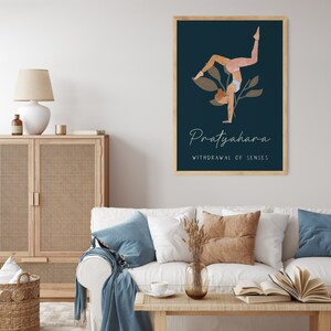 May include: A framed art print featuring a yoga pose illustration against a dark blue background. The artwork includes the word "Pratyahara" and the phrase "Withdrawal of Senses" in elegant script. The print is displayed in a living room setting.