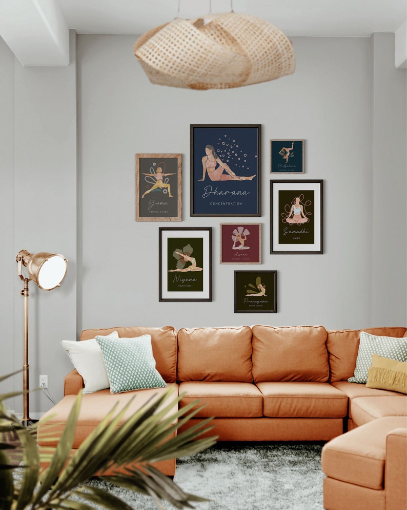May include: A collection of framed yoga art prints displayed on a gray wall above an orange sectional sofa. The prints feature illustrations of yoga poses with text such as "Dharana" and "Samadhi". A woven pendant light hangs from the ceiling.