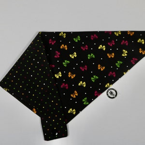 May include: Black dog bandana with a colourful bow pattern on one side and a black polka dot pattern on the other side.