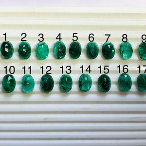 Peut inclure: Dix-sept pierres précieuses d'émeraude de forme ovale, numérotées de 1 à 17, sont présentées sur une surface blanche striée. Les pierres varient du vert foncé au vert clair.