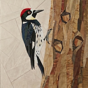 May include: A fabric wall hanging featuring a pieced quilt design of a woodpecker with a red crown, black wings, and white spotted underparts, perched on a textured brown tree trunk against a light beige background with geometric seam lines.