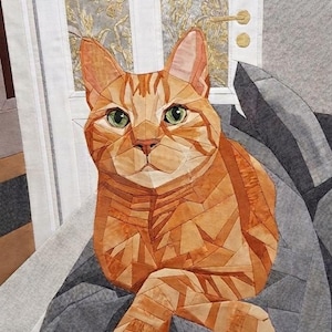 May include: A fabric quilt wall hanging featuring a geometric pieced orange tabby cat with green eyes. The cat is composed of various shades of orange and tan fabric segments, resting on a dark gray textured fabric background with a white door frame.