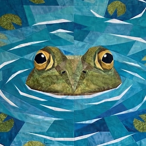 Könnte beinhalten: Ein Stoffquilt mit einem zusammengesetzten Design eines Froschkopfes, der aus blauem Wasser auftaucht. Der Frosch ist in Grün- und Brauntönen mit großen gelben Augen gestaltet. Das Wasser besteht aus verschiedenen blauen Stoffstücken mit weißen Wellen.