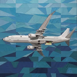 May include: A fabric wall hanging featuring a pieced geometric blue background and a light grey military aircraft appliqué. The aircraft displays the text A47-006 on the fuselage, has two engines, wing-mounted missiles, and an open cargo bay.