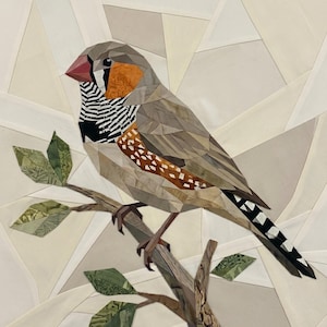 Puede incluir: Una obra de arte de collage de tela que representa un diamante mandarín posado en una rama. El pájaro tiene un pico rojo, una mancha naranja en la mejilla y una garganta a rayas blancas y negras. La rama tiene hojas verdes estampadas.
