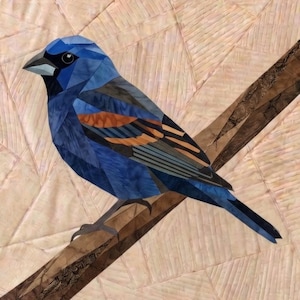 May include: A fabric quilt block featuring a pieced bird with deep blue, light blue, and orange plumage perched on a brown branch. The background consists of light peach and cream fabric pieces arranged in a geometric, angular pattern.