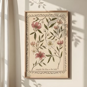 Puede incluir: Un estampado botánico enmarcado con lirios rosas y blancos con hojas y tallos verdes. La obra de arte tiene un fondo beige y un borde decorativo. El texto "consider the lilies in the field" está en la parte inferior.