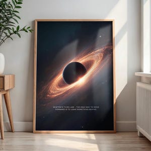 May include: A framed art print featuring a cosmic illustration of a black hole with swirling orange and yellow energy. The print includes the text: "Newton's Third Law - The only way to move forward is to leave something behind."