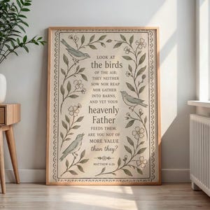 Op de afbeelding: Een ingelijste kunstafdruk met een citaat uit Matteüs 6:26, met de tekst "Kijk naar de vogels in de lucht..." in een decoratief lettertype. Het kunstwerk bevat illustraties van vogels en bloemelementen in gedempte groen- en beigetinten, in een houten lijst.