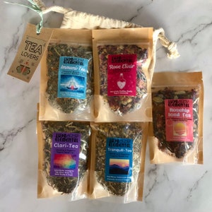 May include: A set of six small pouches of loose leaf tea, each with a different blend and label. The labels are colorful and feature illustrations of flowers, mountains, and a yoga pose. The tea blends are: Rose Elixir, Rosehip Iced Tea, Tranquili-Tea, Clari-Tea, Immuni-Tea, and Rose Elixir.