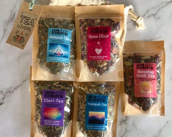 May include: A set of six small pouches of loose leaf tea, each with a different blend and label. The labels are colourful and feature illustrations of flowers, mountains, and a yoga pose. The tea blends are: Rose Elixir, Rosehip Iced Tea, Tranquili-Tea, Clari-Tea, Immuni-Tea, and Rose Elixir.