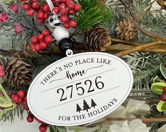 May include: White oval ornament with the text "There's no place like home 27526 for the holidays" with a black and white checkered ribbon and beads.