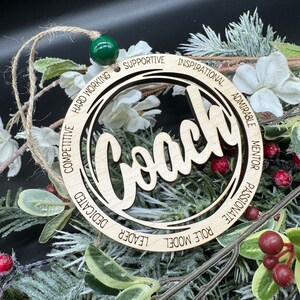 May include: Wooden ornament with the word "Coach" in the center and a circle of words around it, including "Leader", "Role Model", "Passionate", "Mentor", "Admirable", "Inspirational", "Supportive", "Hard Working", "Competitive", "Dedicated".