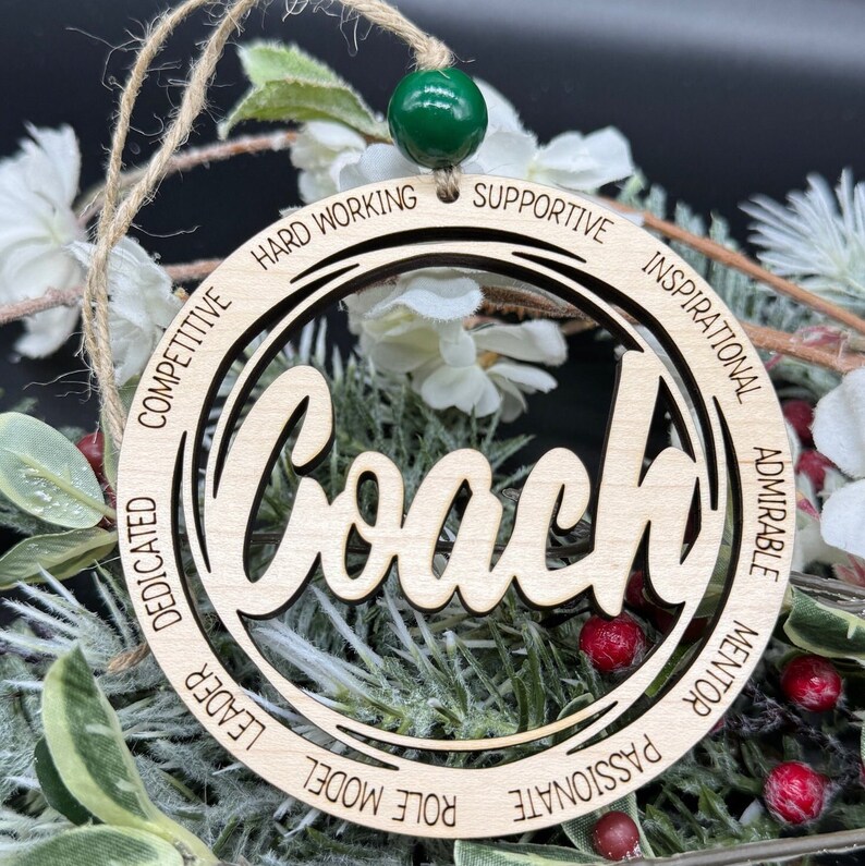 May include: Wooden ornament with the word "Coach" in a cursive font. The ornament is surrounded by a circle with the words "Hard Working", "Supportive", "Inspirational", "Admirable", "Mentor", "Passionate", "Role Model", "Leader", "Dedicated", "Competitive" inscribed around the circle.
