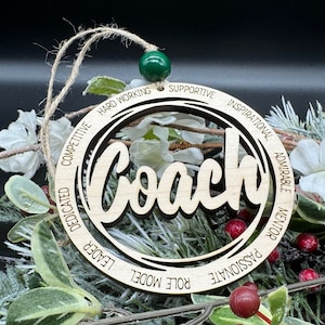 May include: Wooden ornament with the word "Coach" in a decorative font. The ornament is surrounded by a circle with the words "Hard Working", "Supportive", "Inspirational", "Admirable", "Mentor", "Passionate", "Role Model", "Leader", "Dedicated", "Competitive" inscribed around the circle.